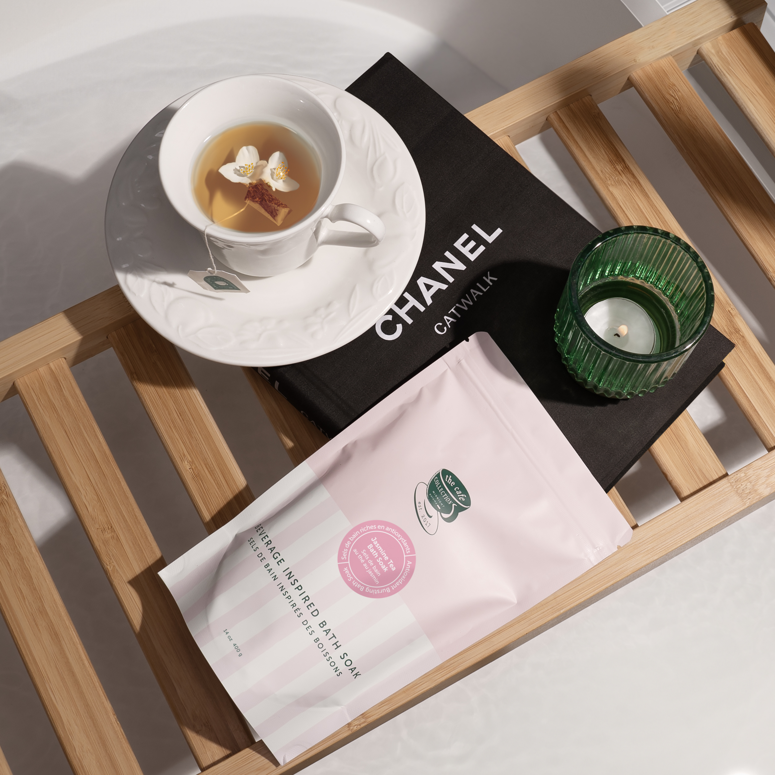 Danielle Gracioso Graphic Designer Vancouver BC Canada –  Flat lay of Jasmine Tea Bath Soak next to a tea cup, green candle, and Chanel book on a bamboo bath tray. Captured and styled by Danielle Gracioso.