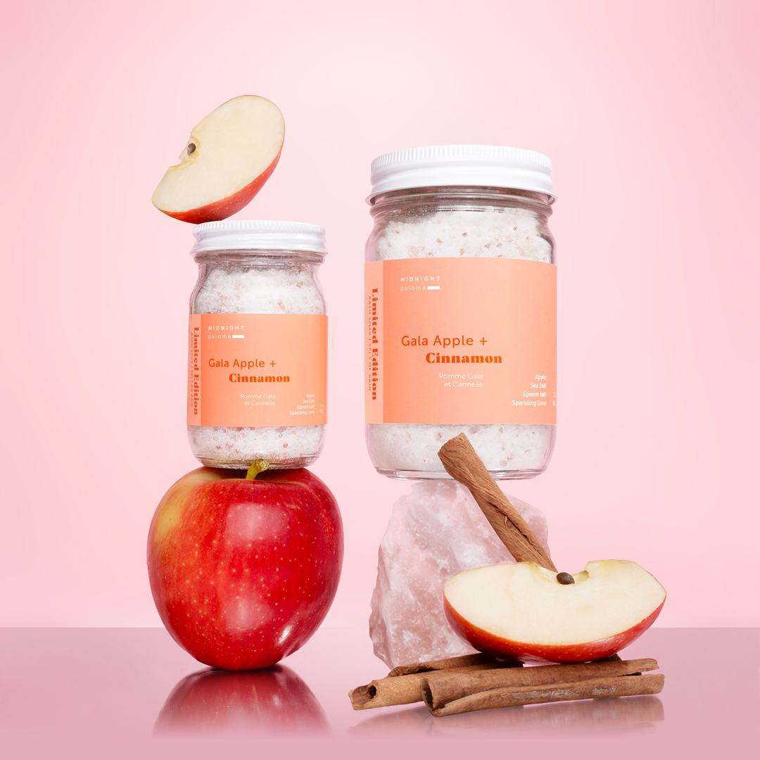 Gala Apple + Cinnamon Bath Soak in glass jars stacked with fresh apple slices, cinnamon sticks, and Himalayan salt. Styled and photographed by Danielle Gracioso.