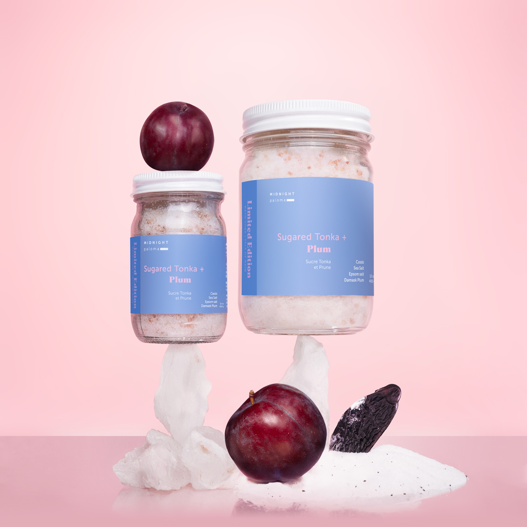 Limited edition Sugared Tonka + Plum Bath Soak in two glass jar sizes, styled with plum, tonka bean and bath salts on a soft pink background. Design and concept by Danielle Gracioso.